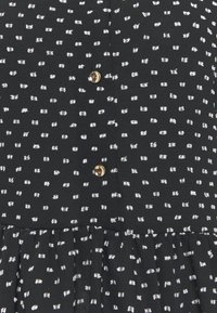 Robe noire à motif moucheté blanc. Présente des boutons dorés et une jupe plissée. Confectionnée en tissu léger.