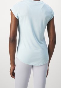 Vaaleansininen lyhythihainen urheilupaita, jossa on kaartuva helma. Valmistettu pehmeästä, kevyestä kankaasta. Hihoissa on hillitty käännettävä yksityiskohta.