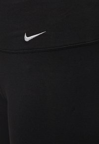 Primer plano de una tela negra con el logotipo de Nike en color blanco bordado por encima de una costura horizontal.