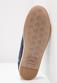 Sole of a blue TOMS slip-on shoe with textured rubber outsole and visible TOMS logo near the heel, photographed upright against a white background.