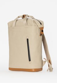 Zaino beige realizzato con materiale resistente, dotato di una maniglia superiore, tasca con zip nera e dettagli marroni sulla parte inferiore e sulle cinghie.
