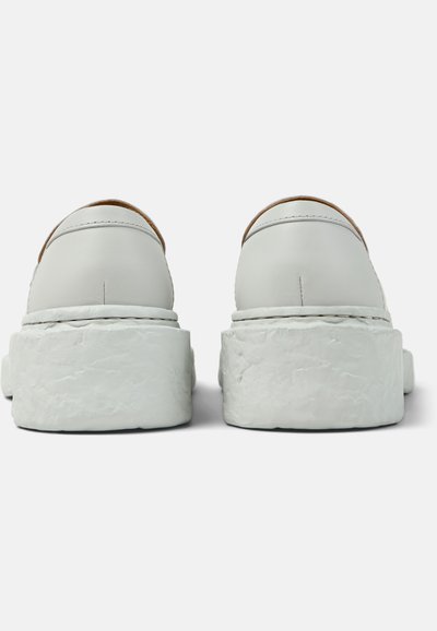 Coppia di scarpe slip-on in pelle bianca con suole platform spesse e testurizzate, viste da dietro su uno sfondo bianco semplice.