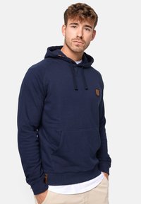 Sudadera azul marino hecha de una mezcla de algodón, con un bolsillo frontal, puños de canalé y un pequeño parche/logo en el pecho.