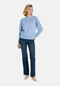 Hellblauer Pullover mit Boot-Ausschnitt, langen Ärmeln und geripptem Saum, kombiniert mit dunklen Jeans und hautfarbenen High-Heels.