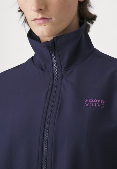 Navy zip-up jacket made of soft fabric with a high collar, featuring a prominent pink "7 DAYS ACTIVE" logo on the chest.