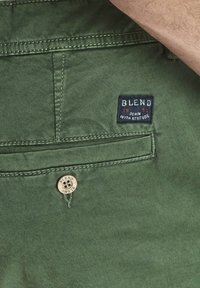 Pantaloni din bumbac verde, având un buzunar la spate, un patch al brandului "BLEND", cusături contrastante și un buton metalic cu detalii gravate.