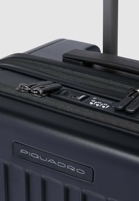 Schwarzer Hartschalenkoffer mit vertikalen Rillen, zwei Reißverschlüssen, Zahlenschloss und ausziehbarem Griff. Verfügt über eine strukturierte Oberfläche.