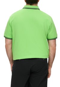 Koszulka polo w jasnozielonym kolorze z krótkim rękawem, kontrastowe czarne wykończenia przy kołnierzyku i rękawach, noszona z czarnymi spodniami.