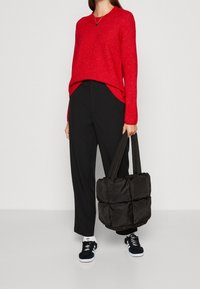 Pull en tricot rouge, coupe ample, pantalon large noir, et sac fourre-tout matelassé noir avec de larges anses, associé à des baskets noires.