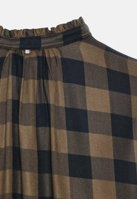 Geruite blouse met een geplooide halslijn. Heeft een houndstoothpatroon in bruin en marineblauw, gemaakt van lichtgewicht stof.