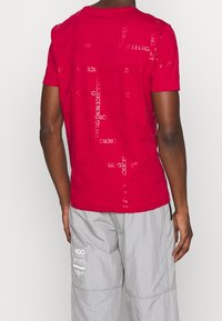 Rotes Kurzarm-T-Shirt mit einem bedruckten Logo-Muster in einer leicht kontrastierenden Textur. Hergestellt aus weichem Stoff in regulärer Passform.