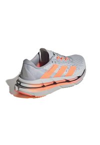 Hellgraue Laufschuhe mit orangefarbenen Akzenten. Strukturierte Oberseite, gepolsterte Sohle und unverwechselbares geschichtetes Design mit sichtbarem Branding an der Seite.