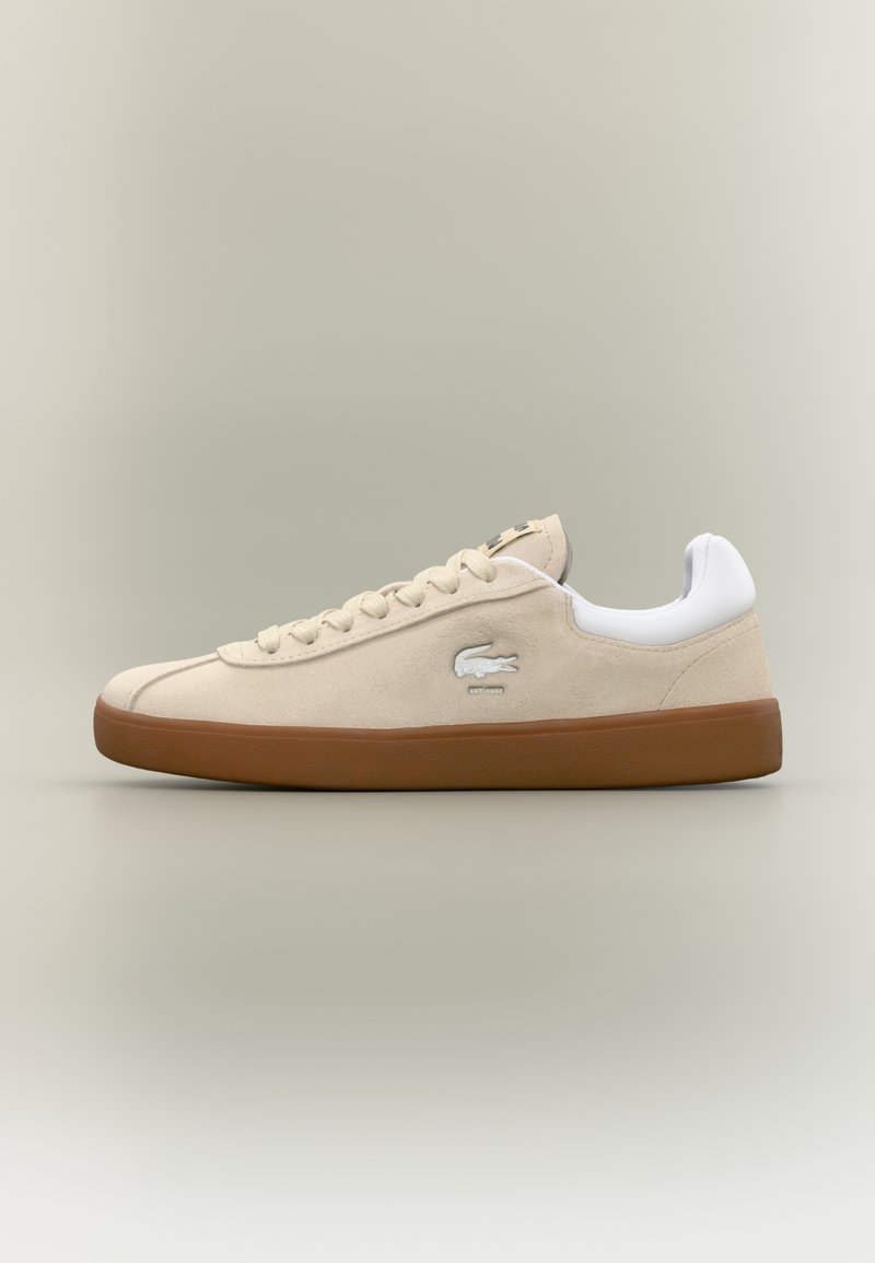 Baskets basses beige avec semelle marron, talon blanc rembourré, lacets à l'avant et logo crocodile sur le côté.