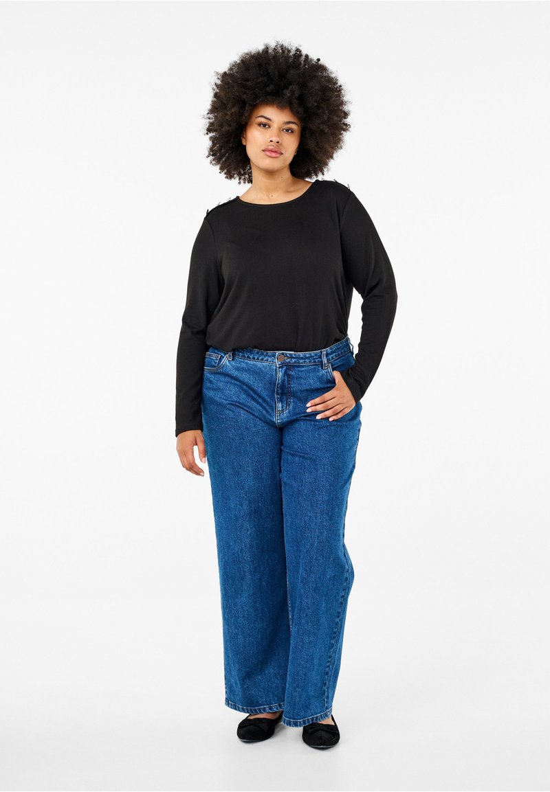 Maglietta nera a maniche lunghe con scollatura rotonda, abbinata a jeans blu a vita alta e larghi. Il modello indossa scarpe balletto nere.