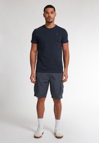 Mørkeblå bomulds t-shirt med rund hals, parret med grå cargo shorts med sidelommer. Hvide sokker og sneakers fuldender udseendet.