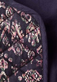 Tessuto trapuntato di un blu navy scuro con un motivo floreale nelle tonalità di rosa e verde. Il design presenta cuciture a rombi e una texture liscia.