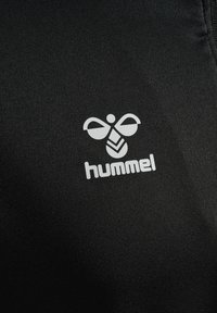 Weißes Hummel-Logo mit stilisierter Biene und Text auf schwarzem, strukturiertem Stoffhintergrund.