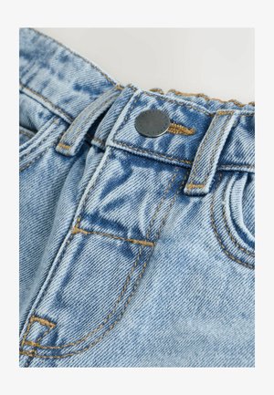 Helehallid teksapüksid, millel on pingutatud vöökoht, metallist nööp ja kontrastsed kollased õmblused, sileda tekstuuriga.