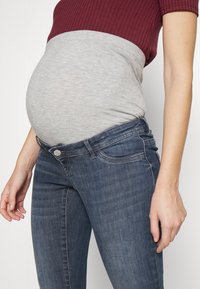 Top de punto gris y marrón con un escote acanalado, combinado con jeans de mezclilla azul oscuro que cuentan con un diseño clásico de cinco bolsillos.