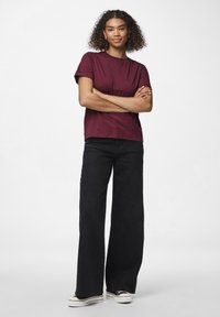 Burgunderfarget T-skjorte med korte ermer, kombinert med vide sorte jeans og svarte sneakers med hvite såler. Glatt stofftekstur.