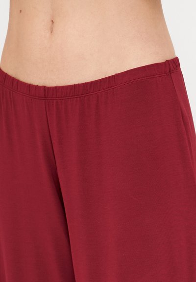 Burgundy soft fabric pants with an elastic waistband, tapering at the ankle. Smooth texture and simple design. No visible patterns or accents.