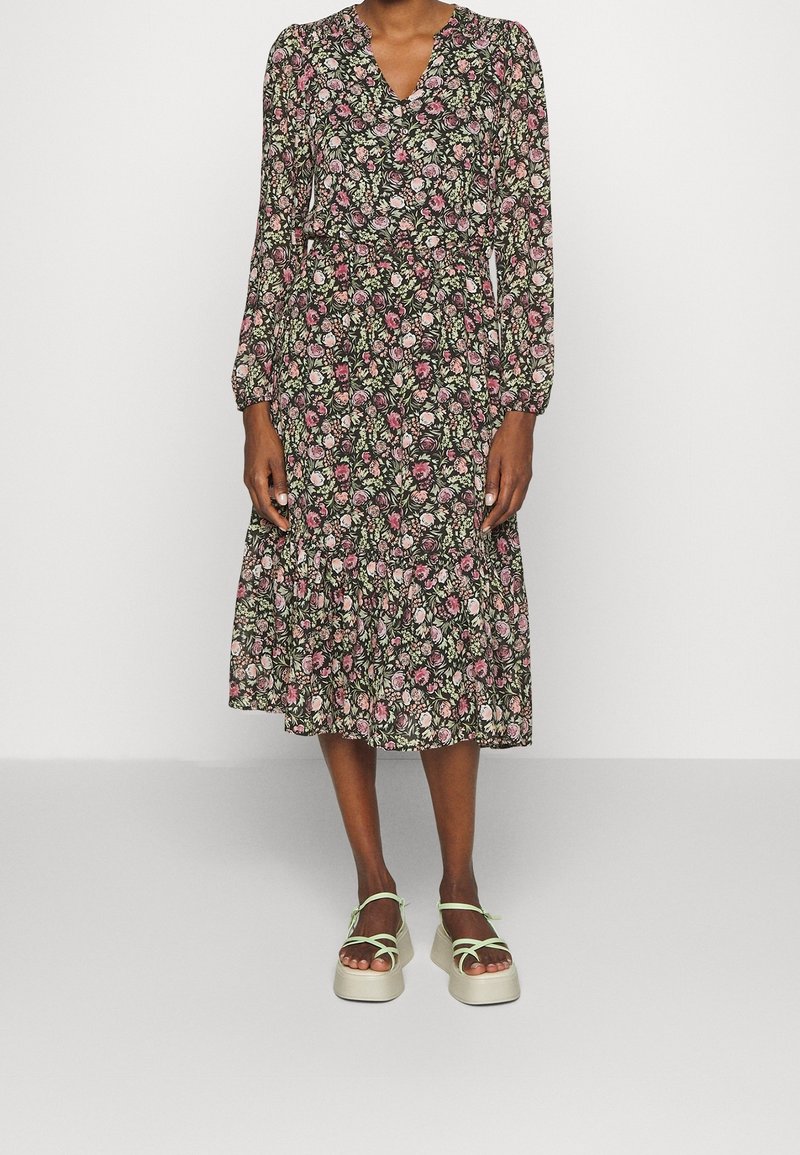 Kukkakuvioinen midimekko mustalla pohjalla, jossa vaaleanpunaisia ja vihreitä kasviaiheisia kuvioita, pitkät hihat, V-aukkoinen pääntie ja kerroksellinen röyhelöreuna. Tarjoaa rentoa istuvuutta.