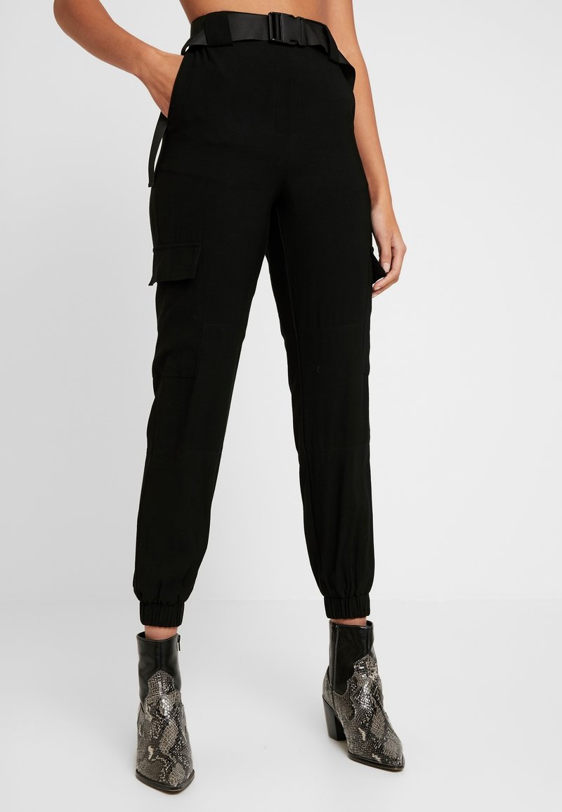 Black cargo pants with a high waistband, front pockets, tapered ankle cuffs, and a belt. Worn with textured black and silver ankle boots.