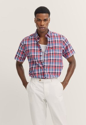 Kurzärmliges kariertes Hemd in Rot, Blau und Weiß mit einem Button-Down-Kragen und einer einzelnen Brusttasche, getragen mit weißen Hosen.