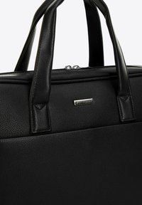 Schwarze Ledertasche mit strukturiertem Finish, ausgestattet mit zwei flachen Tragegriffen, Reißverschluss und silbernem Logo-Akzent.