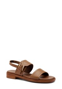 Sandal in pelle marrone con suola piatta, punta aperta e due cinturini larghi. Presenta una piccola fibbia dorata e una soletta testurizzata. Cinturino per il tallone regolabile.