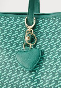 Groene handtas met een patroon, voorzien van een textuur aan de buitenkant, gouden hardware en een hartvormige leren charm aan de rits.