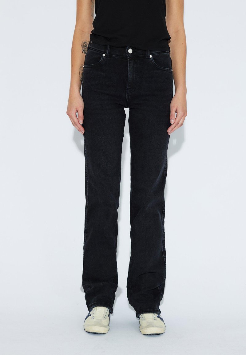 Schwarze Denim-Jeans mit geradem Bein, fünf Taschen, Knopfverschluss und dezenten Steppdetails. Tragen mit hellen Sneakers.
