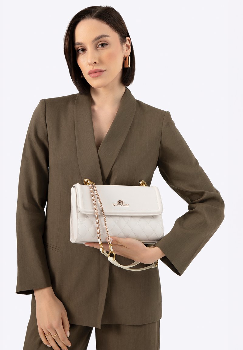 Sac bandoulière matelassé blanc avec des accents en métal doré, doté d'une bandoulière en chaîne. Le sac possède un rabat de fermeture et un logo sur le devant.