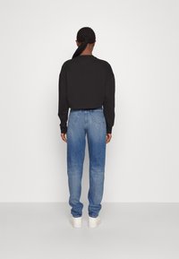 Black cropped sweatshirt paired with light blue high-waisted jeans and white sneakers. The outfit features a relaxed fit and textured fabric.