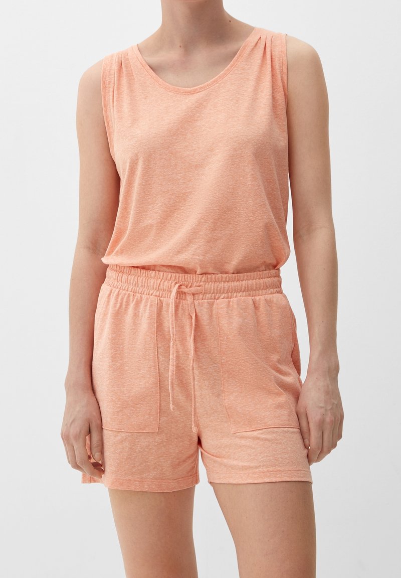 Femme portant un haut sans manches couleur pêche et un short assorti à taille élastique avec cordon et poches avant sur un fond uni.