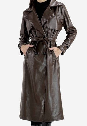 Abrigo largo de cuero marrón oscuro estilo gabardina con cinturón, botones cruzados y detalles de hebillas en las mangas, llevado sobre ropa negra.