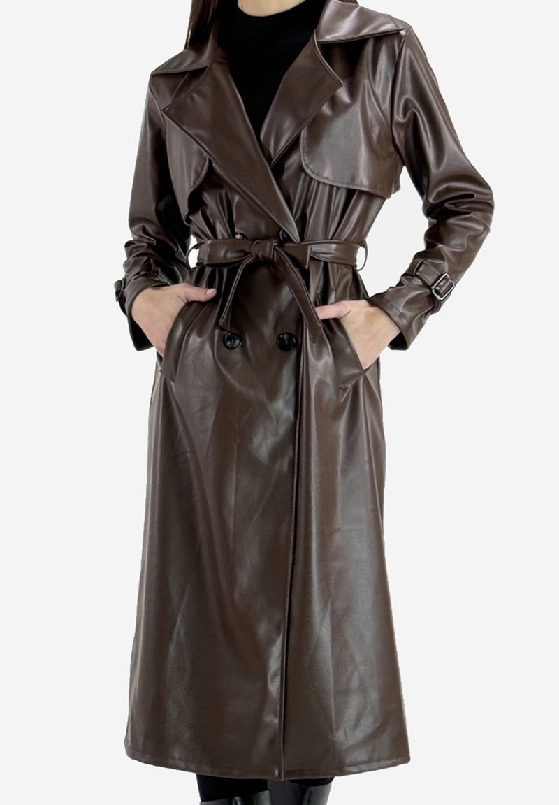 Long trench-coat en cuir marron foncé avec ceinture, boutons croisés et détails de boucles aux manches, porté sur des vêtements noirs.
