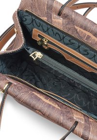 Sac à main marron à motifs ouvert, montrant un intérieur en tissu foncé avec deux compartiments zippés et un revêtement en cuir marron clair.