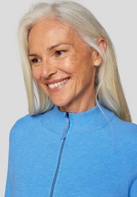 Hellblau gestrickte Zip-Jacke mit hohem Kragen, die eine dezente Textur und einen silbernen Reißverschlussdetail aufweist.