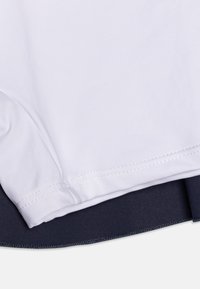 Una camisa blanca con un dobladillo curvado se encuentra sobre una prenda de color azul marino, resaltando los colores contrastantes y las texturas suaves de la tela.