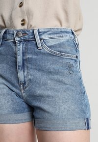 Denimshorts med ljusblå tvätt, texturerat tyg, uppvikta fållar och en liten broderad logotyp framtill. Hållbar söm.