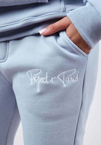 Pantalones deportivos azul claro en tela suave con un logo bordado "Project x Paris", con un bolsillo lateral y detalles de puños acanalados.