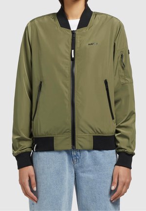 Kurtka typu bomber w oliwkowozielonym kolorze z czarnym kołnierzem, mankietami i lamówką, z przodu zamek błyskawiczny, kieszenie na zamek i małe logo na piersi, noszona z jasnoniebieskimi dżinsami.