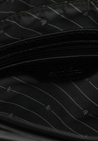 Intérieur en nylon noir d'un sac avec une garniture en cuir noir texturé. Présente une poche zippée et un motif strié subtil en gris.