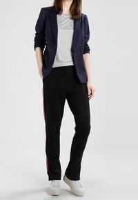 Marineblazer över en grå t-shirt, kombinera med svarta byxor med röda sidostreck och vita sneakers. Slät tyg, skräddarsydd passform.