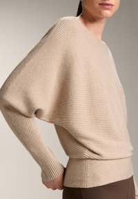 Beige bordázott pulóver laza szabással, széles hajónyakú nyakkal és hosszú ujjakkal. Puha tapintású, ráncolt derékkal.