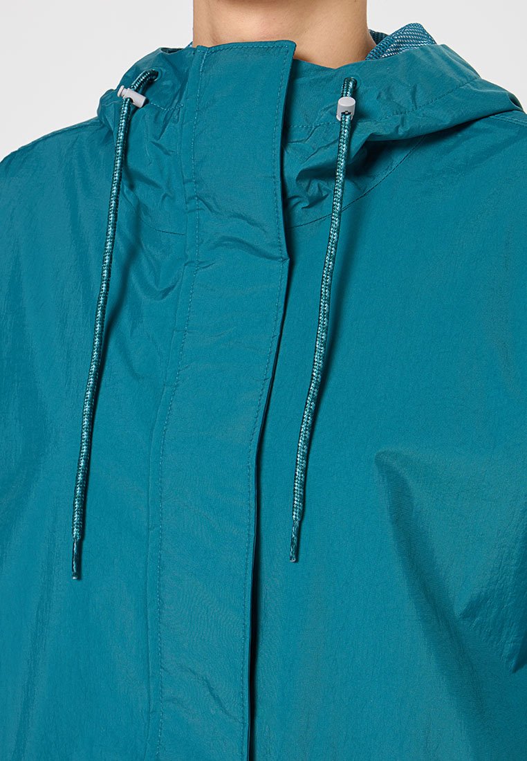 Veste légère teal avec capuche, dotée d'une fermeture éclair à l'avant, de cordons réglables et d'un tissu texturé. Aucuns logos ou motifs visibles.