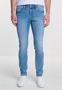 Gai zila džinsu bikses ar slim fit griezumu. Aizņemas pieci kabatas, jostas cilpiņas un pogu aizdare. Apvienotas ar baltām kedām.