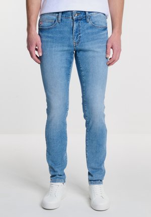 Heledad sinine teksapükste slim-fit lõige. Omab viit taskut, vöölõikeid ja nup closure'd. Kombineeritud valgete tossudega.