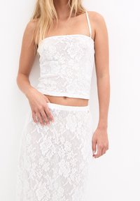 Top corto de encaje blanco con tirantes finos, que presenta un patrón floral. Combinado con una falda de encaje transparente a juego, que muestra una textura en capas.